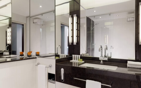 Modernes Badezimmer mit Dusche, Waschbecken und großem Spiegel. Helle Fliesen und bereitgelegte Handtücher.