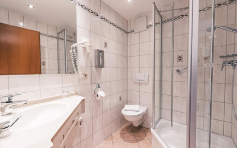 Modernes Badezimmer mit geräumiger Dusche, Waschbecken und großem Spiegel. Helle Fliesen und bereitgelegte Handtücher - Hotel Wartburg in Stuttgart