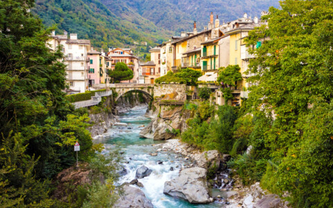 Blick auf die malerische Altstadt von Chiavenna, mit schmalen Gassen, alten Steinhäusern und den umliegenden Alpen im Hintergrund. Eine ruhige Flusslandschaft fließt durch die Stadt.