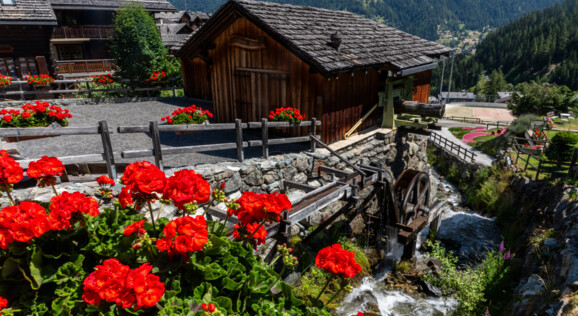 Sonniges Grimentz im Val d’Anniviers mit blumengeschmückten Chalets, malerischen Gassen und atemberaubender Aussicht auf die Walliser Alpen.