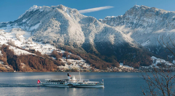 Ein elegantes Schiff gleitet über den Thunersee, umgeben von schneebedeckten Bergen und einer winterlichen Landschaft.