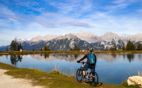 Biker fährt entlang des Kaltwassersees in Seefeld, umgeben von atemberaubender Berglandschaft und klarem, spiegelndem Wasser.