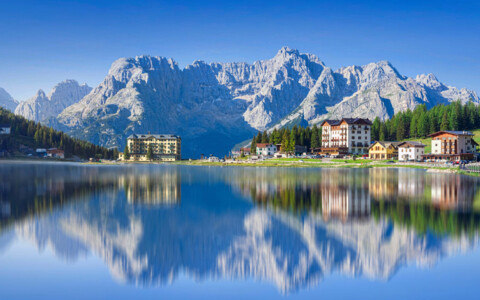 Der malerische Misurinasee in den Dolomiten, umgeben von dichten Wäldern und beeindruckenden Berggipfeln, die sich im klaren Wasser spiegeln.