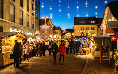 Kunsthandwerk und Geschenke bei Nacht am Weihnachtsmarkt Einsiedeln: Handgefertigte Kunstwerke und einzigartige Weihnachtsgeschenke werden an einem kunstvoll beleuchteten Stand präsentiert, ideal für besondere Mitbringsel.